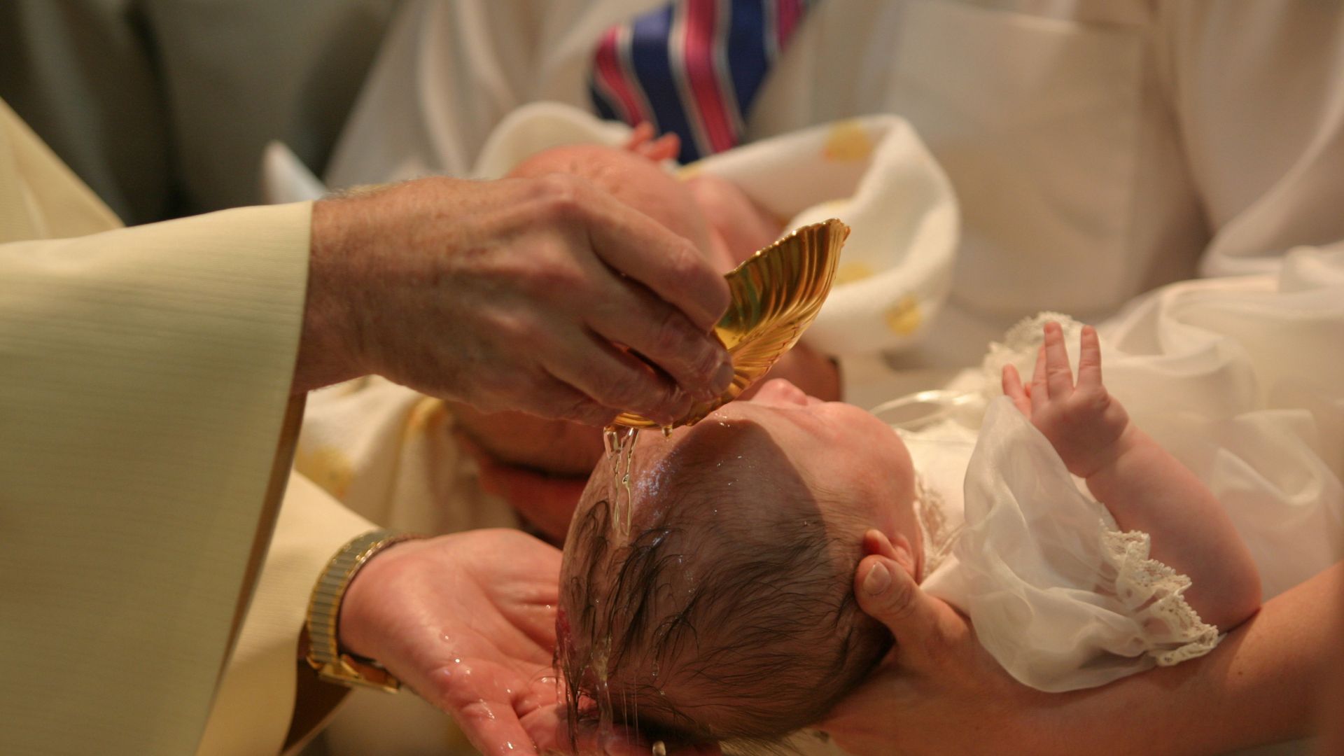 Głowa dziecka polewana wodą przez kapłana – chrzest protestancki praktykuje całkowite zanurzenie głowy.