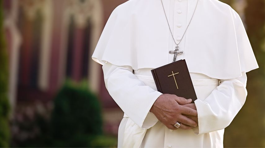 Papież w swoim codziennym ubiorze przechadza się na zewnątrz z Biblią trzymaną w dłoniach.